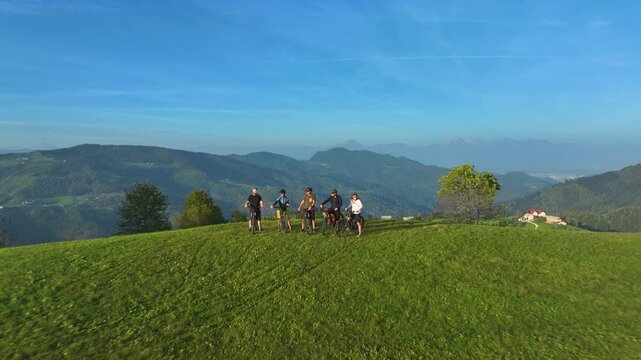 AERIAL: Mountain bikers rest and marvel at the breathtaking nature during a trip in Slovenia. A group of friends cycling in the verdant mountains rest at a scenic viewpoint overlooking the Kamnik Alps
