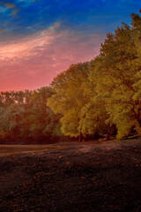 Beautiful sunset. scenery. The sun sets behind the river. Clouds in the evening sky with red, orange, yellow and purple sunlight during the golden hour after sunset, travel concept. green trees.