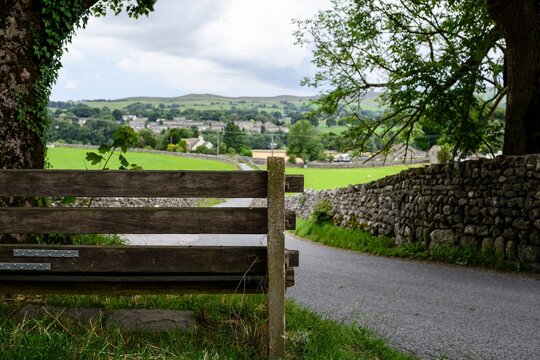 A scenic view of a countryside village with a wooden gate and stone walls under a cloudy sky