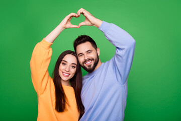 Photo of happy lovely couple wear stylish clothes arms above head heart shape isolated on green color background