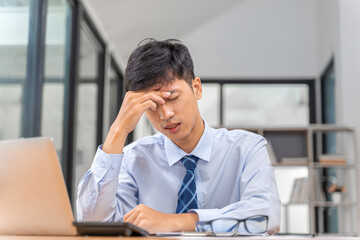 Obraz premium Exhausted young businessman sitting in his office putting his hand on his head trying to ease the pain from his intense headache
