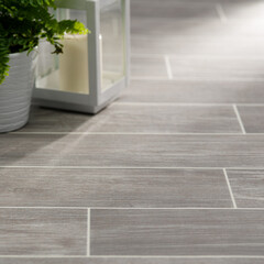 Modern Light Wood-Effect Tile Flooring with Green Plant and Candle Lantern in a Cozy Interior Setting