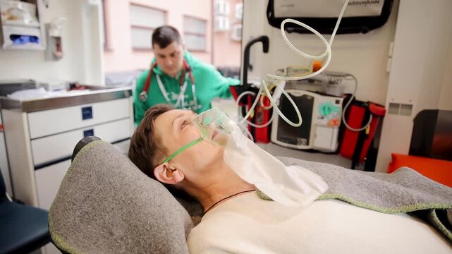 Close up of female patient breathing through oxygen mask. Support in ambulance next to heart rate machine. Mature woman breathing with oxygen air supply