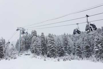 Cabins of the chairlift against the background of mountains and forests on a gray winter cloudy day.