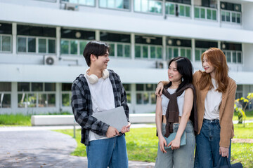 Three young people are standing outside a building, smiling and holding books