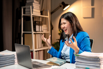 A woman in a blue jacket is sitting at a desk with a laptop