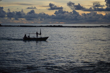 Fototapeta premium A peaceful scene of a boat silhouetted against a stunning sunset, with a backdrop of dramatic clouds over a calm sea, evoking a sense of serenity and adventure.