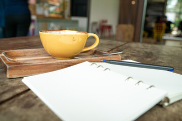Hot latte coffee cup on wood table with blank notebook