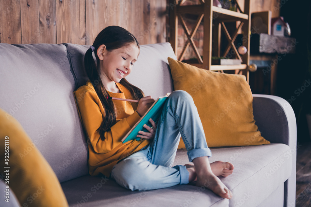 Wall mural Full size photo of cute small girl sit couch write notebook dressed orange outfit cozy day light home interior living room