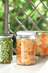 Tasty pickled vegetables and mushrooms in jars on white table indoors