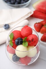 Tasty watermelon and melon balls with blueberries in glass on white table, closeup