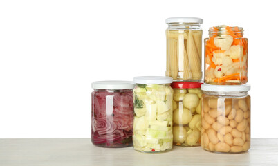 Different pickled products in jars on light wooden table against white background