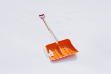 An orange plastic snow shovel lying in the snow. Winter time.