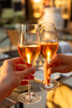 Couple celebrating at dinner time, hands while toasting with glasses of orange moscato wine in outside restaurant during golden hour. Vertical image...