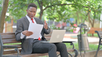 African Man Shocked with Business Report with Laptop in Lap Outdoor