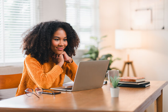 African American woman smiles while watching laptop screen at home.