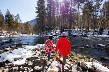 Children, brother and sister, in the mountains by a snow-covered river.