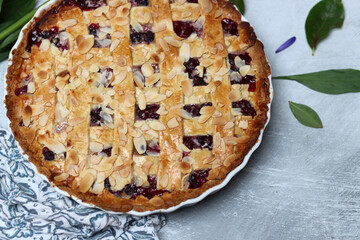 Delicious homemade pie with blueberries and almonds, summer flowers and leaves on light background, top view photo of fresh pastry item 