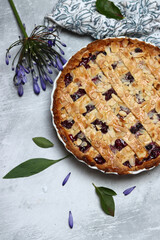 Homemade lattice cherry pie with almonds and blue flowers on a light background with space for text. 