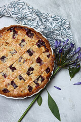 Homemade lattice cherry pie with almonds and blue flowers on a light background with space for text. 