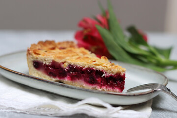 Plate with a piece of cherry pie and flowers on a light background with space for text. Homemade pastry item. 