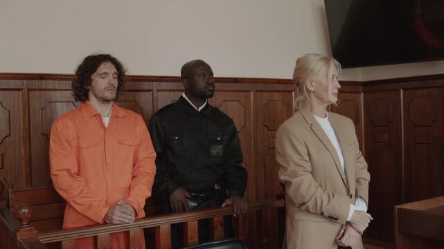 Female attorney, policeman and male suspect standing and listening to judge passing verdict at court hearing