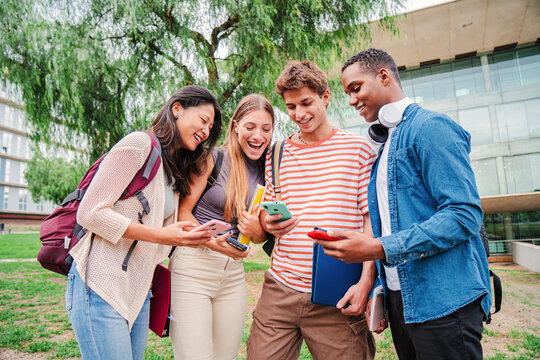 group of students happily sharing content on social media using a cellphone app. friends engrossed in their smartphones. Multiracial teenagers browsing the internet on campus with their mobile phones - Powered by Adobe