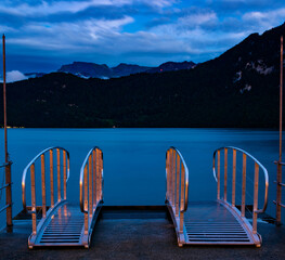 View from a jetty at lake Lucerne with two catwalks. Mountains in the background.