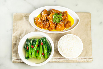 Sesame Chicken in Lemon Sauce with baby kailan and white rice served in dish isolated on napkin top view of asian food
