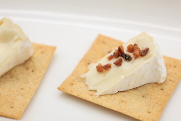 白い皿に盛ったクラッカーの上に切ったカマンベールチーズを乗せ、トッピングを加えたモノ