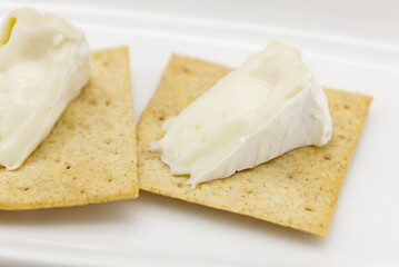 白背景のクラッカーの上に切ったカマンベールチーズをのせたモノ