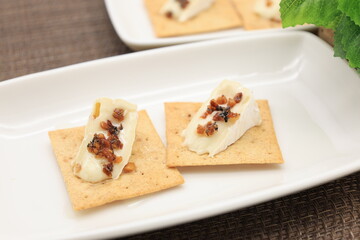 白い皿に盛ったクラッカーの上に切ったカマンベールチーズを乗せ、トッピングを加えたモノ