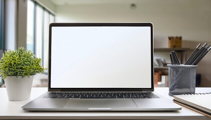 Fototapeta premium Modern workspace with an open laptop displaying a blank screen, a plant, and office supplies on a desk in a bright, spacious room.