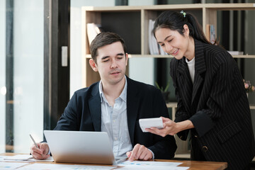 A man and a woman are sitting at a desk with a laptop and a tablet