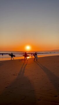 Surfers on the background of Vivid sunset, Surfing golden hour, beach atlantic ocean, Portugal, Costa da Caparica