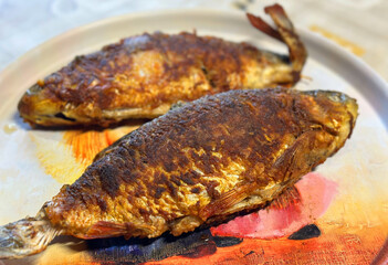 Fried fish on a plate on the table. Fish after smoking on fire. Smoked fish cooked on smoke in a smokehouse.