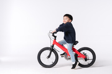 Obraz premium Asian child riding a red bicycle with a playful expression in a studio setting.