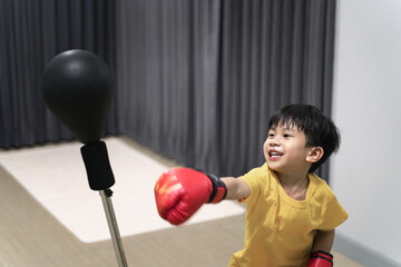Young boy in a yellow shirt practicing boxing with a punching bag, wearing red boxing gloves.