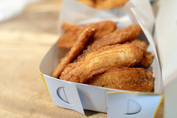 Close-up of crispy fried banana slices in a takeaway box.