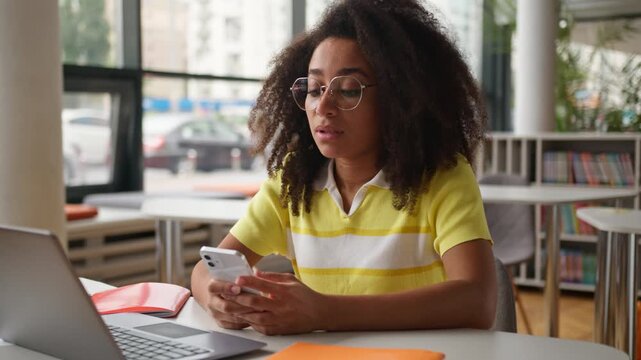 Thinking pensive worried thoughtful African American ethnic girl female student business woman businesswoman looking at mobile phone chatting smartphone in cafe with laptop school university library