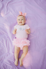 baby girl in pink dress lay on purple background