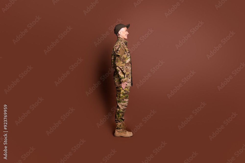 Sticker Full length photo of pensioner lady professional officer stand profile dressed camouflage army uniform isolated on brown color background