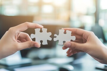 Two hands carefully connect matching puzzle pieces in a blurred office setting, symbolizing teamwork and problem-solving