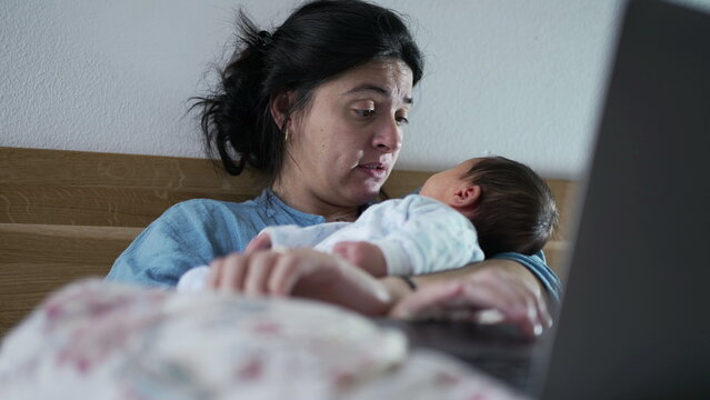 Woman multitasking with a laptop and newborn baby in a cozy bedroom setting, exemplifying the balance between work and parenting, modern family dynamics, and nurturing maternal love