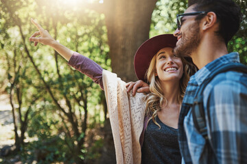 Couple, pointing and happy in forest on adventure with smile to explore nature, bonding and love in...