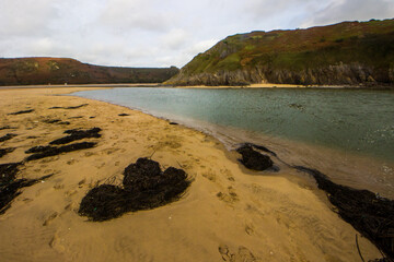 Pennard Pill stream where it flows over the sandy beach at Three Cliffs Bay in Wales on an overcast day.