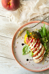 plate with caprese salad with peaches, mozzarella and basil on the table