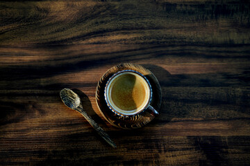 Vintage coffee cup and palm wooden spoon dark theme under sunlight