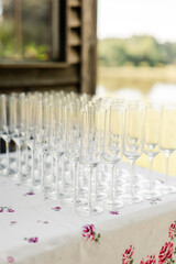 Rows of empty champagne glasses on a floral tablecloth outdoors

