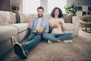Obraz premium Full length portrait of two nice young people eat chips watch tv raise fist weekend modern apartment indoors